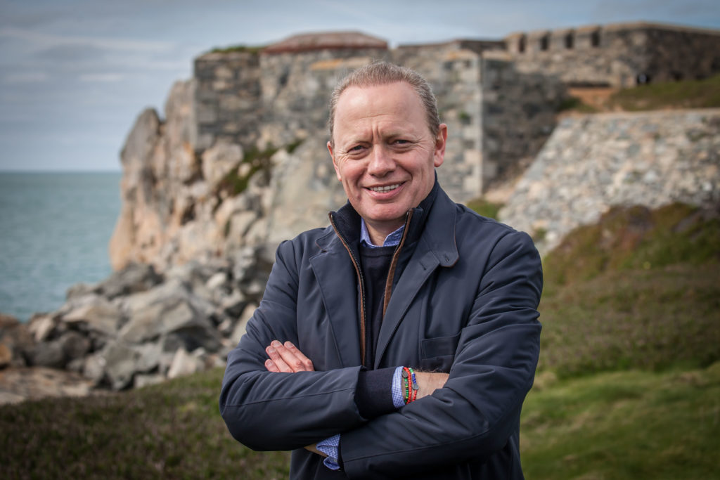 A man with his arms crossed in front of a castle.