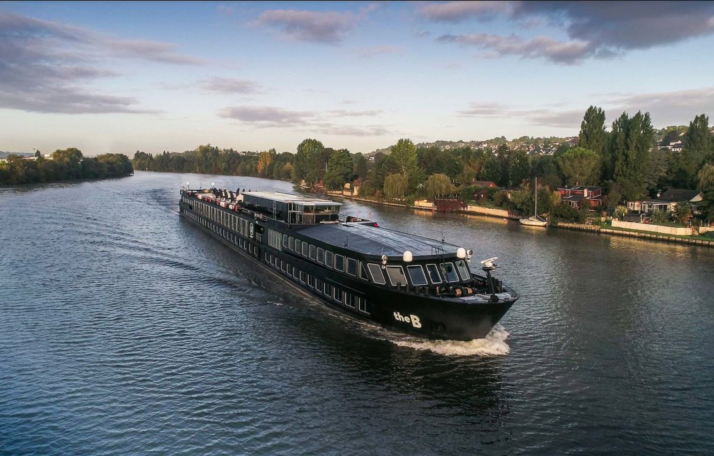 A large black boat is traveling down a river.
