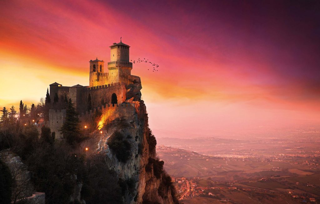 A castle sits on top of a mountain at sunset.